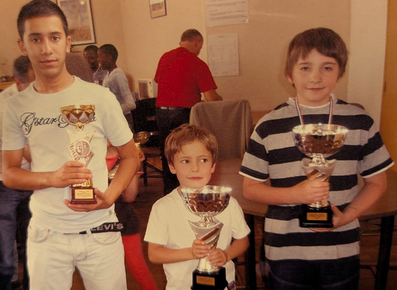 Three young chess players holding their trophies after a championship; Remy Machado is the one on the right, in the striped shirt
